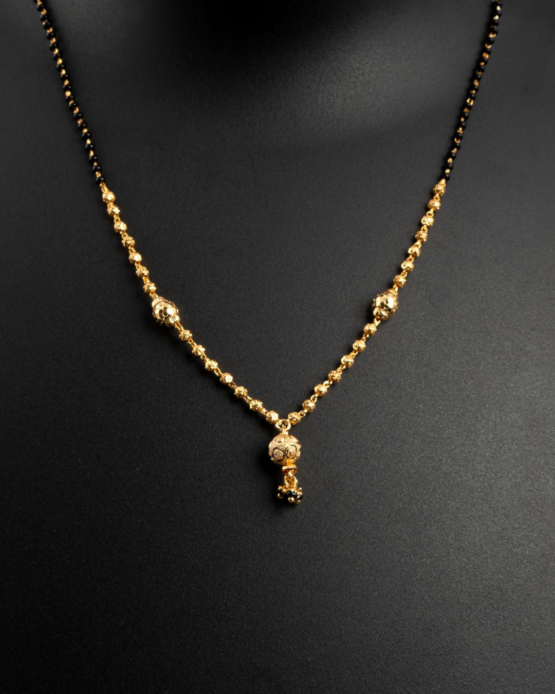 Gold necklace with a small pendant on a black background